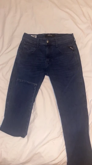 Replay blå jeans med raka ben - Snygga blå jeans från Replay med klassisk femficksdesign och raka ben. Jeansen har mörk tvätt, tydliga sömmar och Replay-logga på bakfickan samt läderpatch i midjan. Materialet är mjukt jeans och passformen är normal, perfekt för en chill stil.