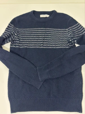 Blå randig stickad tröja Pier One - Mörkblå stickad tröja från Pier One i storlek S. Tröjan har vita horisontella ränder över bröstet och ett snyggt strukturmönster. Rund halsringning och ribbade muddar vid ärmslut och nederkant. Perfekt för dig som gillar klassisk men modern stil.