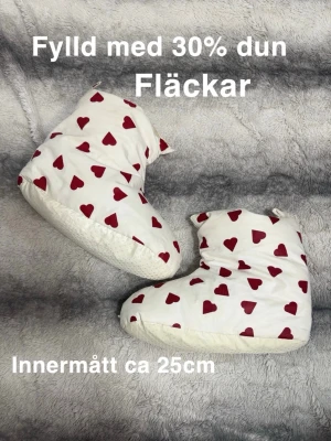 Vita tofflor med röda hjärtan - Mysiga vita tofflor fyllda med 30% dun och dekorerade med röda hjärtan. Perfekta att glida runt i hemma när det är kallt. De har en mjuk och fluffig känsla och en halkfri sula undertill.🌸 Fläckar. Fylld med 30% dun. Innermått ca 25cm vilket enligt skotabell skulle motsvara ca storlek 38
