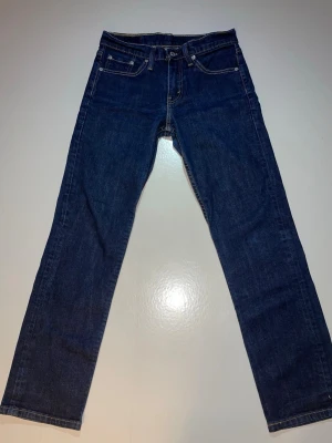 Levi's 511 mörkblå jeans W29 L30 - Snygga mörkblå Levi's 511 jeans med klassisk femficksdesign och raka ben. Jeansen har kontrastsömmar, knapp och dragkedja i gylfen samt den ikoniska Levi's-lappen bak. Perfekt passform och stilren look för dig som gillar tidlösa jeans.