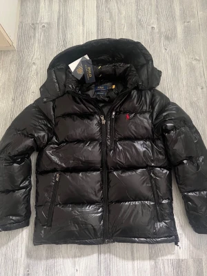 Ralph lauren jacka - Hej! En glossy Ralph lauren jacka till salu. Jackan är i jättebra skick och den har inga defekter elller tecken av användning. Jackan är köpt på Nk och kvittot finns kvar. Jag säljer jackan pågrund av att den tyvärr inte passar mig, priset kan diskuteras lite vid snabbaffär. hör av dig vid frågor 😁