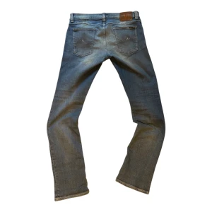 Nudie jeans - Säljer ett par blå jeans från Nudie med snygga slitningar på benen och fickorna. Jeansen har klassisk femficksdesign, raka ben och slim passform. Perfekta för dig som gillar en avslappnad och trendig look.