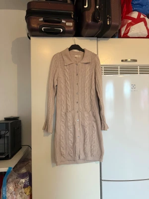 Beige lång kofta med kabelstickning - Säljer en beige lång kofta med snygg kabelstickad design, stora fickor framtill och knappar hela vägen. Koftan har krage och långa ärmar med ribbade muddar. Perfekt för dig som gillar mysiga och stilrena plagg. Från märket Odd Molly. Storlek 3 som enligt deras storleksguide motsvarar en L. Mycket fint skick, jag hittar inga synliga anmärkningar eller defekter. 