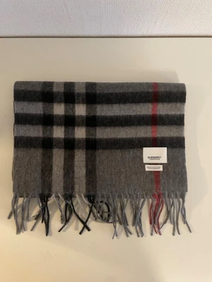 Grå rutig Burberry kashmir scarf -  Burberry Classic Cashmere Scarf. Lyxig, mjuk kashmir, vävd i Skottland. Svart/grått rutmönster med röda detaljer. Levereras i originalförpackning med kvitto – perfekt present! 