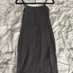 Mörkgrå ribbad klänning - Säljer en enkel och stilren mörkgrå ribbad klänning. Klänningen har smala axelband och en rak, kroppsnära passform. Använd 1 gång