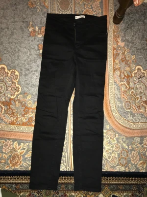 Svarta Perfect Jeans Molly Gina Tricot L - Svarta Perfect Jeans Molly från Gina Tricot i storlek L. Byxorna har en klassisk femficksdesign, dragkedja och knapp framtill. De är tighta och har en hög midja, tillverkade i stretchigt bomullsmaterial för en bekväm passform.