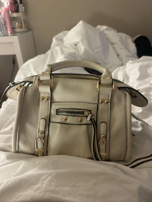 Beige handväska med gulddetaljer  - Snygg beige handväska i skinn med guldfärgade detaljer. 