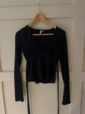 Mörkblå från Nelly XS - Mörkblå från Nelly i storlek XS. Toppen har lång ärm, v-ringning och knytband i midjan. Materialet är ribbat och ger en snygg struktur. Perfekt att styla med jeans eller kjol för en trendig look.