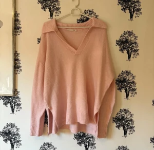 Ljusrosa stickad tröja från Lager 157 - Supermysig ljusrosa stickad tröja från Lager 157 med bred krage och v-ringad hals. Tröjan har långärmade, loose passform och ribbade detaljer vid krage, ärmslut och nederkant. Perfekt för dig som gillar chill och oversized stil.