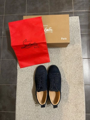 Mörkblå Christian Louboutin Skor - Snygga mörkblå sneakers från Christian Louboutin i mocka med klassisk röd sula och rund tå. Skorna har snörning och platt sula, och kommer med originalkartong, dustbag och äktighets bevis. Skicket är 9/10 för man kan se att dom e använda. Skriv vid funderingar 🧩