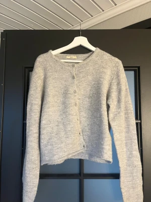 Ljusgrå stickad kofta från Gina Tricot - Supermjuk ljusgrå stickad kofta från Gina Tricot i storlek L. Koftan har rund halsringning, långa ärmar och knäppning framtill med matchande knappar. Perfekt för lager-på-lager och chill vibes.