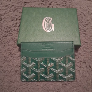 Grön plånbok med mönster - Snygg grön plånbok med det klassiska grafiska mönstret i vitt och brunt. Plånboken har flera kortfack och är tillverkad i skinn. Perfekt för dig som vill ha en lyxig och stilren accessoar med Paris-vibe.