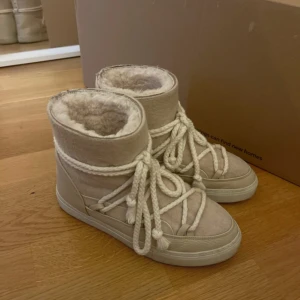 Beige moon boots från Inuikii - Säljer ett par beige moon boots från Inuikii med fluffigt foder och grova snören som detaljer. Skorna har en platt sula och är tillverkade i skinn och syntet med guldiga nitar bak. Perfekta för kalla dagar och riktigt snygga till vinterlooken. Sparsamt använda så i mycket fint skick!