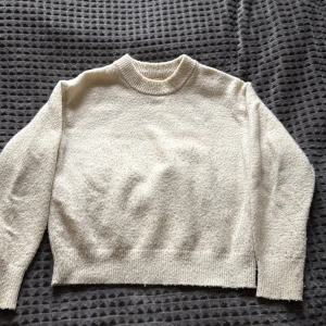 Beige stickad tröja Gina Tricot - Mysig beige stickad tröja från Gina Tricot med rund hals och ribbade muddar vid ärmslut och nederkant. Tröjan har en enkel, klassisk design och är långärmad, perfekt för kyliga dagar. Passar dig som gillar stilrena och bekväma plagg.