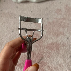 Ögonfransböjare med rosa handtag - Säljer en ögonfransböjare i metall med snygga rosa handtag i plast. Perfekt för att få till en riktigt fin böj på fransarna. Greppvänlig design som gör den enkel att använda och passar i sminkväskan! 