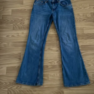 Blå bootcut jeans från 157, M - Snygga blå jeans från 157 med bootcut passform och låg midja. Klassisk femficksmodell med kopparfärgade nitar och kontrastsömmar. Jeansen är tillverkade i jeansmaterial och har en cool, lite tvättad look. Perfekt för dig som gillar retrovibbar och breda ben.