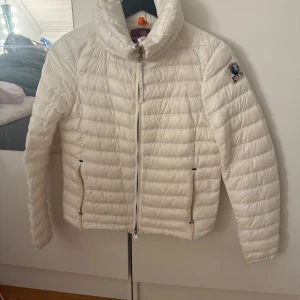 Vit dunjacka Parajumpers XS - Snygg vit dunjacka från Parajumpers i modellen Hollywood. Jackan har quiltad design, hög krage och dragkedja framtill samt två fickor med dragkedja. Perfekt för kyliga dagar och riktigt clean look.