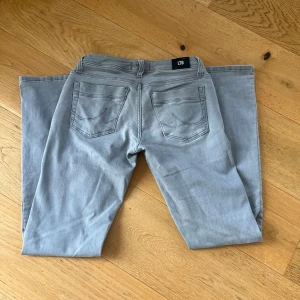 Grå Valerie jeans från LTB med utsvängda ben - Snygga grå jeans från LTB med utsvängda ben. Jeansen har silverfärgade nitar vid fickorna och snygga sömmar på bakfickorna. Har används men är fortfarande i fint skick.   Är i storlek 28/32. Men har sytt in midjan så att det passar 26/27. (Midjemått: 36cm rakt över) Hör av dig om det är något!