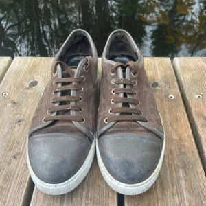 Bruna sneakers i mocka med svart tå - Snygga bruna sneakers med ovandel i mocka och svart tåparti i gummi. Skorna har rund tå, snörning och vit platt sula. Perfekt för dig som gillar en stilren och klassisk look med lite edge. Passar till jeans och hoodie eller en chill outfit.