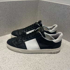 Valentino Garavani svartvita sneakers - Svartvita sneakers från Valentino Garavani med coola nitar på sulan. Skorna har snörning, rund tå och platt sula. Tillverkade i skinn med kontrasterande vit panel på sidan och vit häl. Märkeslogga på plösen och detaljerad yttersula. Det saknas 4 spikar på båda skorna 