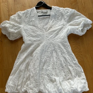Vit kortklänning med broderade blommor från ZARA - Superfin vit kortklänning från ZARA med puffärmar och djup v-ringning. Klänningen har ett detaljerat blommigt broderi över hela tyget och är tillverkad i ett lätt, luftigt material🤍