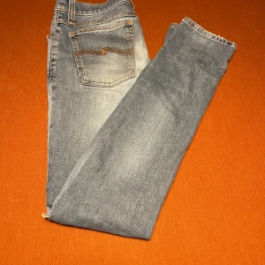 Nudie jeans - Snygga blå jeans från Nudie med broderad bakficka och slitna detaljer på benen. Jeansen har klassisk femficksdesign, normal passform och är tillverkade i mjukt bomullsmaterial. Perfekt för dig som gillar en avslappnad och cool stil.