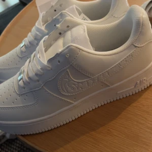 Vita sneakers i Air Force-stil strl 41 - Snygga helvita sneakers i klassisk Air Force 1-stil från iSNRBED. Skorna har rund tå, platt sula och är gjorda i syntetmaterial med perforerade detaljer framtill. Tidlös design med snörning och diskret logga på sidan. Perfekta för dig som gillar cleana och stilrena sneakers.