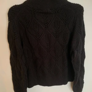 Svart stickad polotröja med mönster - Säljer en svart stickad polotröja med snyggt hålmönster i hela tröjan. Tröjan har hög krage och långa ärmar, perfekt för kyliga dagar. Den har en lite loose passform och ribbade muddar vid ärmslut och nederkant.