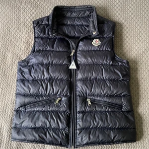 Moncler väst - Säljer nu min moncler väst då det börjar bli för liten, jag är 165 cm lång.                                                           Snygg mörkblå dunväst från Moncler med quiltad design och hög krage. Västen har två praktiska fickor med dragkedja och klassisk Moncler-logga på bröstet. 