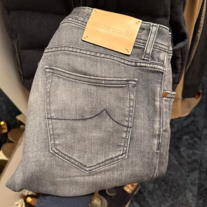 Jacob Cohën jeans  - Snygga grå jeans från Jacob Cohën i modellen Bard, med skinny passform och klassisk femficksdesign. Jeansen har en mörkgrå tvätt, knappgylf med logotyp, och detaljerad insida med mönstrat tyg. Perfekta för dig som gillar stilrena och moderna jeans.
