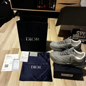 Grå Dior sneakers med mesh och skinn - Säljer ett par grå Dior sneakers med snygga meshpaneler och detaljer i skinn. Skorna har rund tå, platt sula och snörning. Insidan är vit med Dior-logga och yttersulan har CD-märkning. Kommer med originalkartong, dustbag och kvitto.