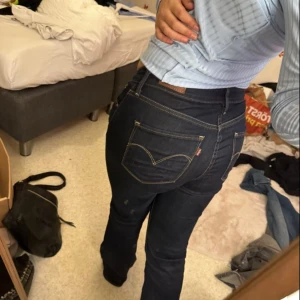 Levi's Demi Curve Bootcut Jeans blå - Säljer ett par mörkblå Levi's Demi Curve jeans i bootcut-modell med klassisk midja. Jeansen har snygga kontrastsömmar, fem fickor och klassisk Levi's-logga på bakfickan. Perfekt passform och riktigt sköna att bära. OBS jeansdn har en liten fläck på låret som knappt syns av bronzer
