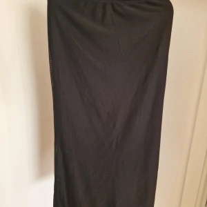 Svart långkjol i tunn bomull - Enkel och stilren svart långkjol i tunn bomull. Kjolen har rak passform och resår i midjan, vilket gör den bekväm och lätt att bära. Perfekt för dig som gillar minimalistisk stil och vill ha något som funkar till många olika looks. Helt oanvända 
