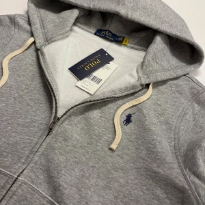zip up hoodie från Polo Ralph Lauren - Snygg zip up hoodie från Polo Ralph Lauren. skick är 10/10 och aldrig använd. Tillverkad i mjuk bomullsmix, perfekt för chill dagar eller när du vill ha en clean look. Passar dig mellan 165-175. Ny pris runt 2300.