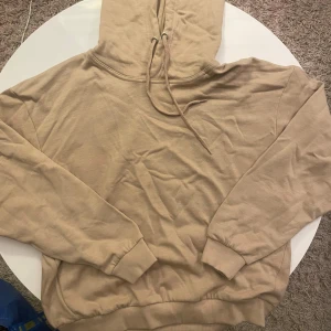 Beige hoodie från 157 med huva - Säljer en beige hoodie från 157 i storlek M. Tröjan har huva med snörning, ribbade muddar vid ärmslut och nederkant samt en klassisk loose passform. Perfekt för chill dagar eller när du vill ha en enkel och stilren look.