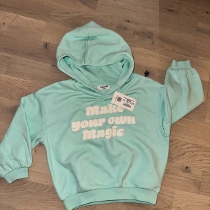 Mintgrön hoodie från Kappahl med tryck - Superfin mintgrön hoodie från Kappahl med vit text 'Make your own Magic' framtill. Tröjan har huva, långa ärmar och ribbade muddar. Perfekt för dig som gillar färg och coola tryck.Mintgrön hoodie från Kappahl med texten "Make your own magic" i vitt. Tröjan har en huva och muddar vid ärmslut.