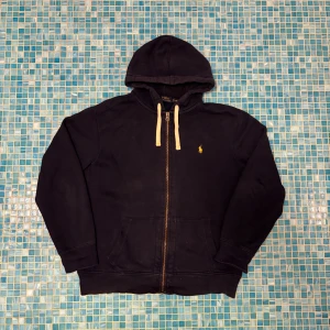 Navy hoodie från Polo Ralph Lauren XL - Navy hoodie från Polo Ralph Lauren i storlek XL. Klassisk design med dragkedja, huva med vita snören och gult broderat logomärke på bröstet. Tillverkad i mjuk bomull och har två stora fickor framtill. Perfekt för chill dagar eller när du vill ha en clean streetstyle.