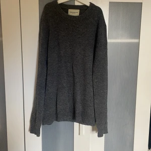 Mörkgrå stickad tröja These Glory Days - Mörkgrå stickad tröja från These Glory Days i storlek M. Tröjan har en enkel, rund halsringning och långa ärmar. Materialet är mjukt och har små färgstänk i rött och blått som ger en cool touch. Perfekt för dig som gillar stilrena och bekväma plagg.