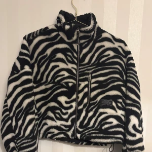 Zebramönstrad teddyjacka från Bershka - Säljer en fluffig teddyjacka från Bershka med svartvitt zebramönster. Jackan har hög krage, hel dragkedja framtill och en bröstficka med dragkedja. 