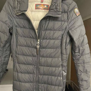 Grå dunjacka Parajumpers S - Säljer en superlätt och snygg grå dunjacka från Parajumpers i storlek S. Jackan har quiltad design, dragkedja framtill och klassisk logga på ärmen. Perfekt för kyliga dagar och har en stilren look som funkar till det mesta.