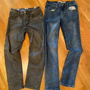 Två par smala jeans i blått och grått - Säljer två par jeans, ett par i klassisk blå tvätt och ett par i mörkgrått. Båda har femficksmodell, smal passform och normal midja. Perfekta för dig som gillar en enkel och stilren look. Materialet är mjukt jeans-tyg med lite stretch för extra komfort.
