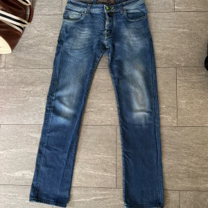 Jacob Cohen 622  - Snygga Jacob Cohen 622 Comfort jeans i mörkblå tvätt med coola slitningar och kontraststickningar. Klassisk femficksmodell med gröna detaljer och knappgylf. Slim passform och stretchigt jeanstyg för extra komfort. Perfekt för dig som gillar stilrena och trendiga jeans. Har en lagning i skrevet men den syns inte. Midjebredd 40,5cm, ytterbensmått 105cm. Hör av dig vid minsta fråga eller fundering! 