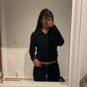 Svart stickad v-ringad tröja Polo Ralph Lauren - Svart stickad tröja från Polo Ralph Lauren med v-ringning och diskret röd broderad logga på bröstet. Tröjan har långärmad passform och ribbade muddar vid ärmslut och nederkant. Perfekt för dig som gillar klassisk och stilren look. Aldrig använd 🌸