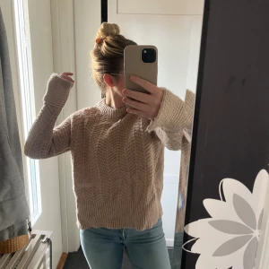 Beige stickad tröja med mönster - Mysig beige stickad tröja med snyggt strukturmönster och ribbade muddar. Tröjan har lång ärm och en lite lösare passform, perfekt för lager på lager. Rund halsringning och lätt upphöjd nederkant bak för en cool look.