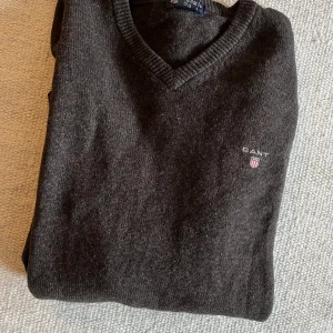 Mörkbrun stickad tröja från Gant - Mysig mörkbrun stickad tröja från Gant med v-ringad hals. Perfekt för lager-på-lager och passar till allt. Klassisk och stilren design som funkar året runt.