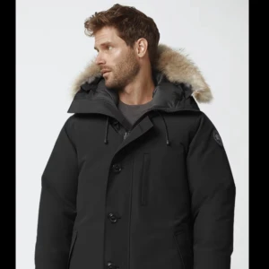 Svart parka från Canada Goose - Svart parkas från Canada Goose med huva och äkta pälsdetalj. Jackan har stora knappar, dragkedja, snörning vid kragen och flera fickor. Klassisk patch på ärmen. Perfekt för kalla dagar och riktigt snygg siluett. Köpt 2024, använd en vinter. Kvitto finns. Black Label Chateau Parka.