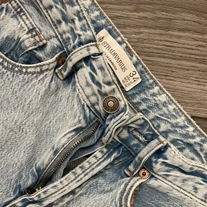 Ljusblå raka jeans från Stradivarius - Säljer ett par ljusblå jeans från Stradivarius i storlek 34 med petite passform.  Jeansen har klassisk femficksdesign, raka ben och dragkedja med knapp framtill. De är tillverkade i denim med snyggt tvättad look och har bälteshällor i midjan. 