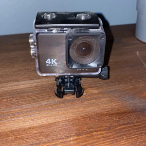 4K Ultra HD Actionkamera - Actionkamera med 4K Ultra HD-upplösning, levereras i vattentätt hus med fäste. Utrustad med HDMI och microSD-port. Kameran är i gott skick med mindre ytliga repor på linsen och huset, men inga synliga större skador. Den kommer inte med minneskort och är aldrig använd, skriv vid frågor eller funderingar.