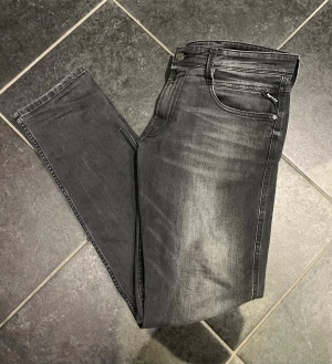 Replay svarta slim jeans - Snygga svarta Replay jeans med slim passform och klassisk femficksdesign. Jeansen har en lätt tvättad look med grå toner och detaljerade sömmar på bakfickorna. Materialet är stretchigt jeans och midjan är normal. Perfekt för dig som gillar stilrena och moderna jeans. Anbass slim fit. Storleken är 33