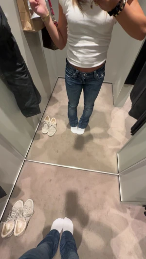 Miss Me jeans med broderad bakficka - Säljer ett par blå Miss Me jeans med snyggt broderad bakficka och glittriga detaljer. Jeansen har dekorativa knappar, kontrastsömmar och en klassisk femficksmodell. Materialet är slitstarkt denim och passformen är normal med raka ben.